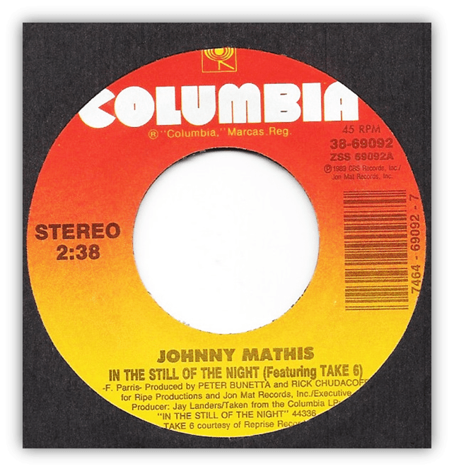A vinyl record label showing Columbia at the top and details for Johnny Mathiss song In the Still of the Night (Featuring Take 6). The text is red and yellow with black lettering.