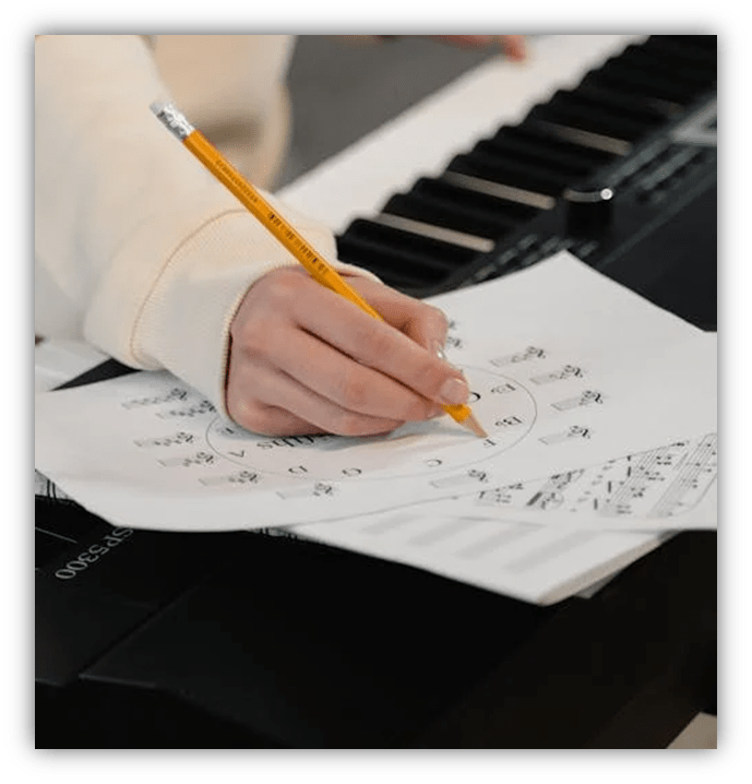 Person writing with a pencil while seated at a keyboard.