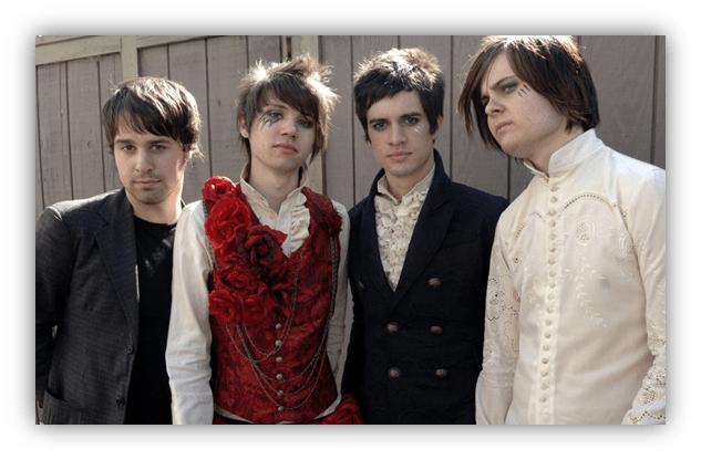 Four members of a rock band pose together outdoors, showcasing a mix of edgy and vintage fashion styles. The first member on the left wears a dark blazer, while the second features a striking red vest adorned with roses. The third member is dressed in a black suit, and the fourth sports a white, intricately designed shirt. A wooden fence serves as the backdrop.