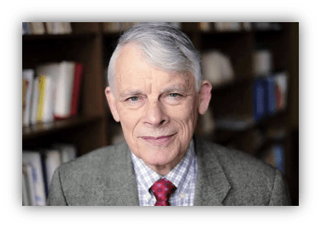 Portrait of an older man with gray hair, wearing a gray blazer and a red tie, smiling confidently in front of a bookshelf filled with books.