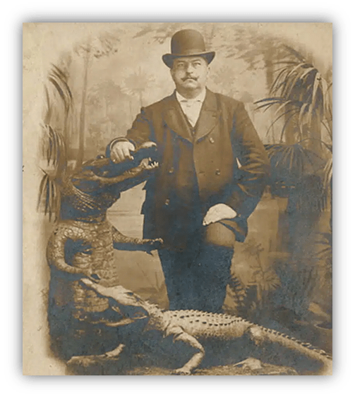 Victorian man in a bowler hat poses with taxidermy crocodiles in a vintage photograph.