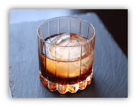 "Glass of whiskey with ice on a slate surface."