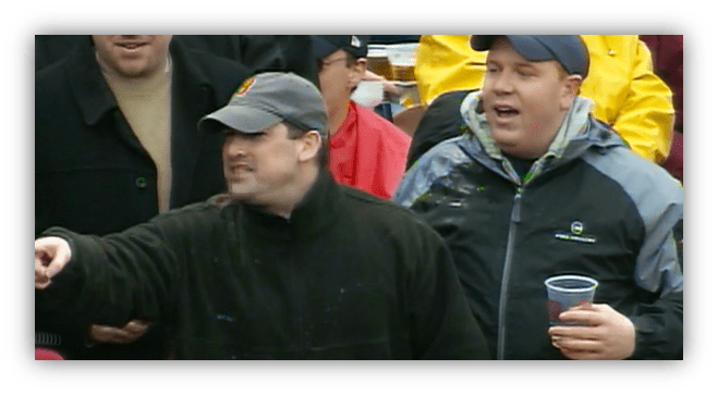 Cheering fans at a sporting event, one man pointing and another holding a drink.