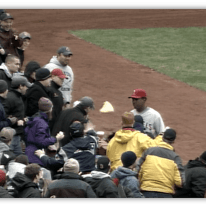 Baseball fans interacting with a player on the field during a game.