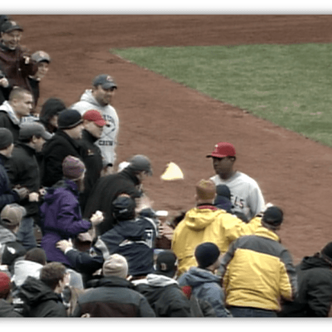 Baseball fans interacting with a player on the field during a game.