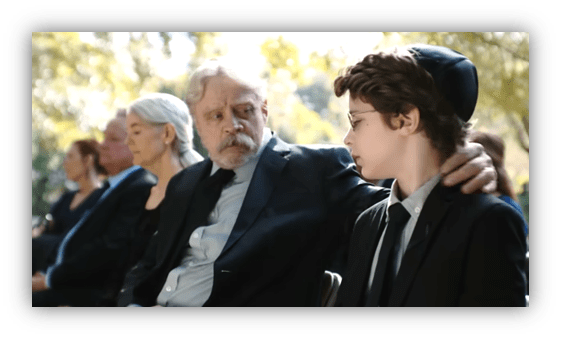 Elderly man comforts a young boy at a somber outdoor gathering.