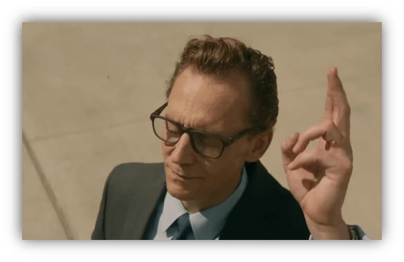 Businessman in a suit with glasses, gesturing confidently outdoors.