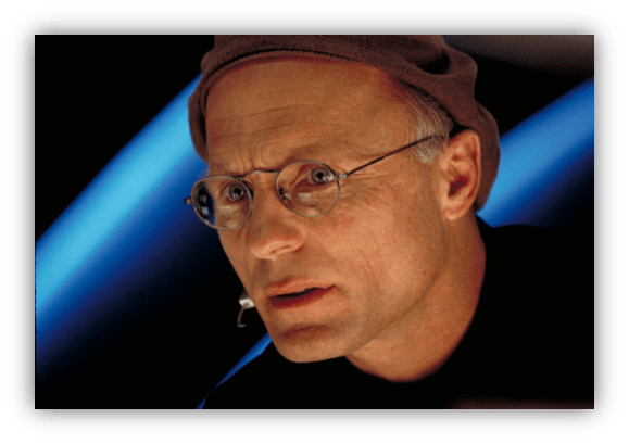 Close-up of a man with glasses and a cap, focused expression, against a blue background.