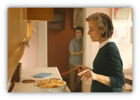 "Woman cooking in the kitchen with a boy watching from the doorway."