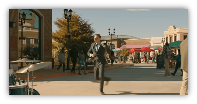 Businessman running through a busy outdoor shopping area with people and colorful umbrellas.