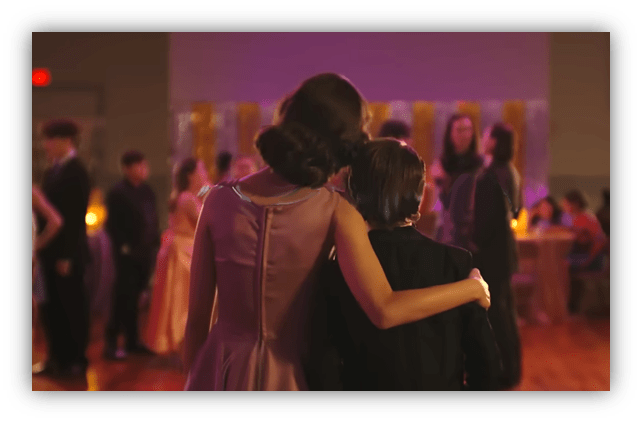 "Two young dancers embracing at a formal event, surrounded by a festive atmosphere."