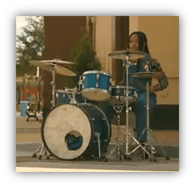 Young drummer performing on a blue drum set outdoors.