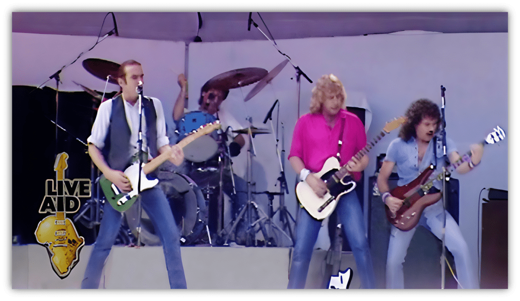 "Live Aid performance featuring a rock band on stage with guitars and drums."