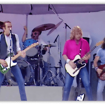 "Live Aid performance featuring a rock band on stage with guitars and drums."