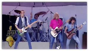 "Live Aid performance featuring a rock band on stage with guitars and drums."
