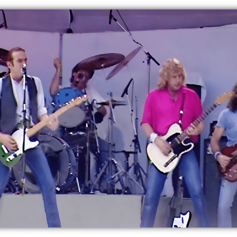 "Live Aid performance featuring a rock band on stage with guitars and drums."