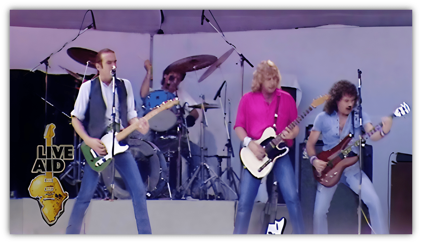 "Live Aid performance featuring a rock band on stage with guitars and drums."