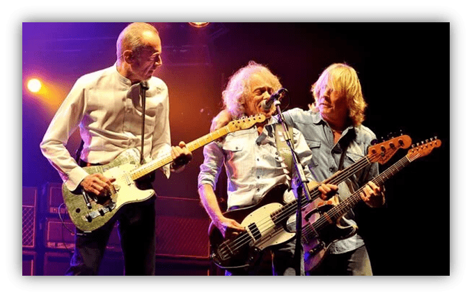 "Three musicians performing on stage with electric guitars under stage lights."