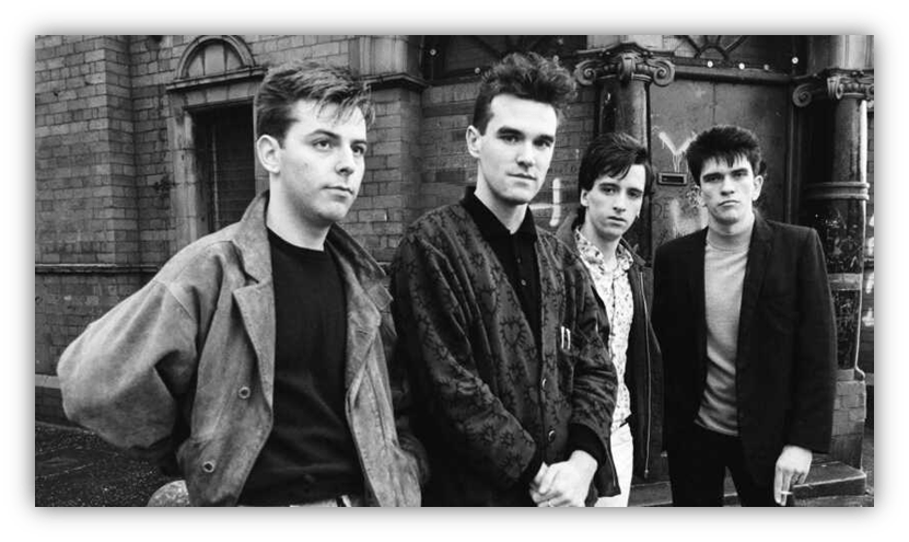 "Black and white photo of four young musicians posing outside a brick building."