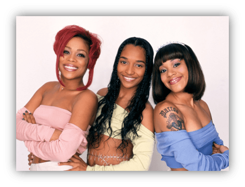 Three women posing together, showcasing vibrant hairstyles and stylish outfits.