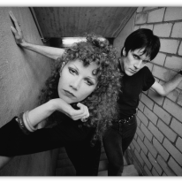 Black and white photo of a couple posing in a stairwell, showcasing edgy fashion and dramatic expressions.