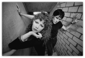 Black and white photo of a couple posing in a stairwell, showcasing edgy fashion and dramatic expressions.