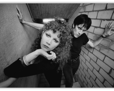 Black and white photo of a couple posing in a stairwell, showcasing edgy fashion and dramatic expressions.