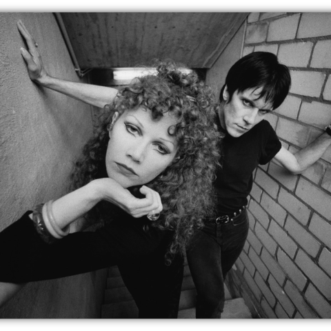 Black and white photo of a couple posing in a stairwell, showcasing edgy fashion and dramatic expressions.