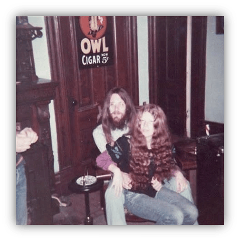 "1970s couple with long hair sitting in a vintage room, featuring a cigar advertisement."