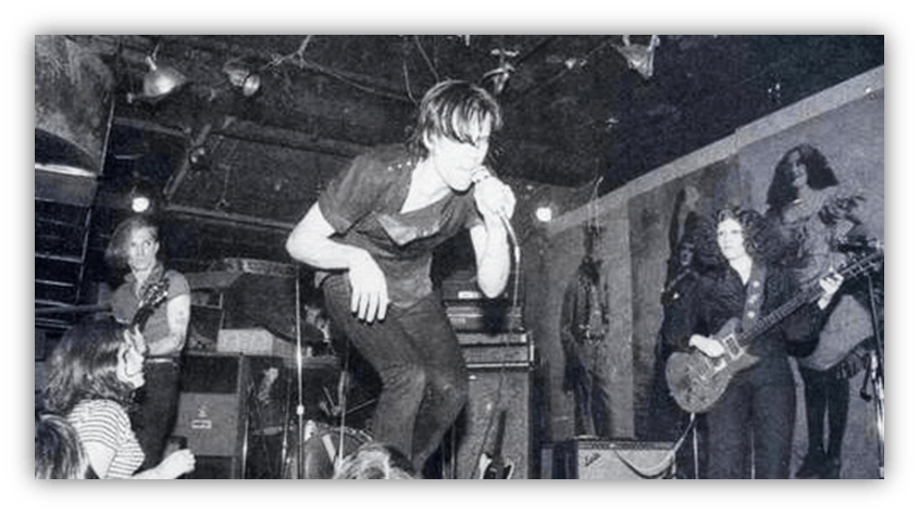 "Black and white photo of a live rock band performing on stage, with an energetic singer and musicians engaging the audience."