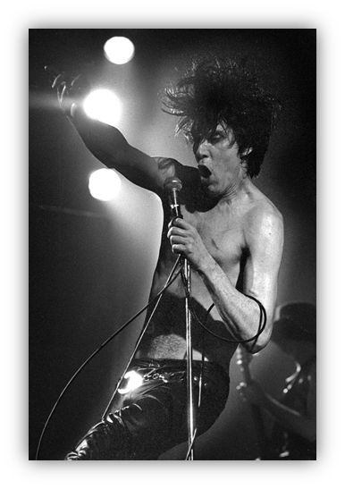 "Black and white image of a shirtless male rock singer passionately performing on stage with a microphone."