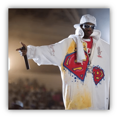 Rapper performing on stage in oversized Superman-themed hoodie and sunglasses.