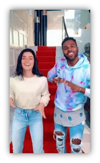 Two friends dancing on a red carpet staircase, wearing casual outfits.
