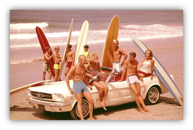 "Group of young surfers with surfboards by a vintage Mustang on the beach."