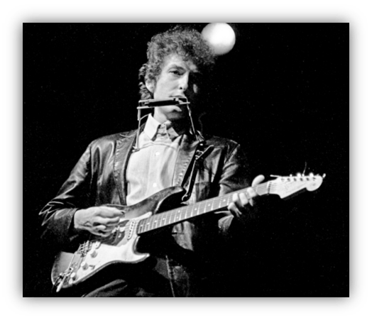 Bob Dylan performing with guitar and harmonica on stage.