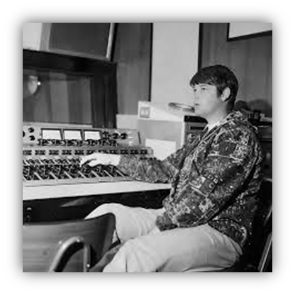 "Black and white photo of a young man operating a music mixing console in a recording studio."