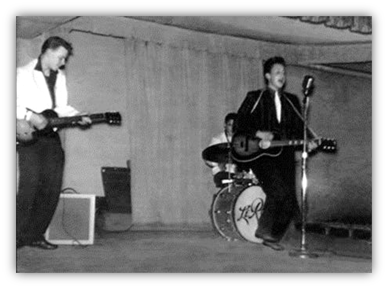 Black and white image of a live band performing on stage, featuring a guitarist, a singer with a guitar, and a drummer.