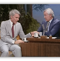 Steve Martin and Johnny Carson share a moment on The Tonight Show, seated at a talk show desk.