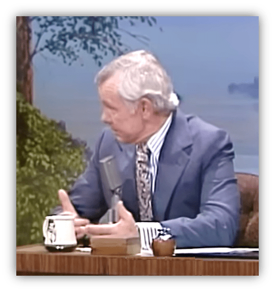 "Classic talk show host discussing a topic at a wooden desk with a microphone."