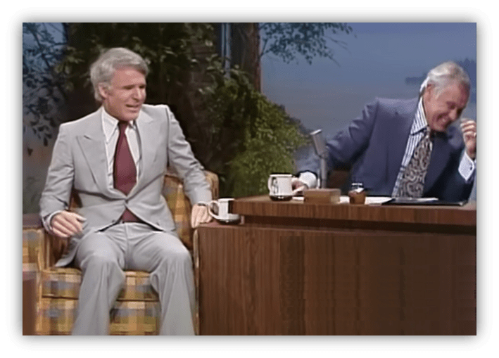 "Classic talk show moment with a guest in a suit and the host laughing at the desk."