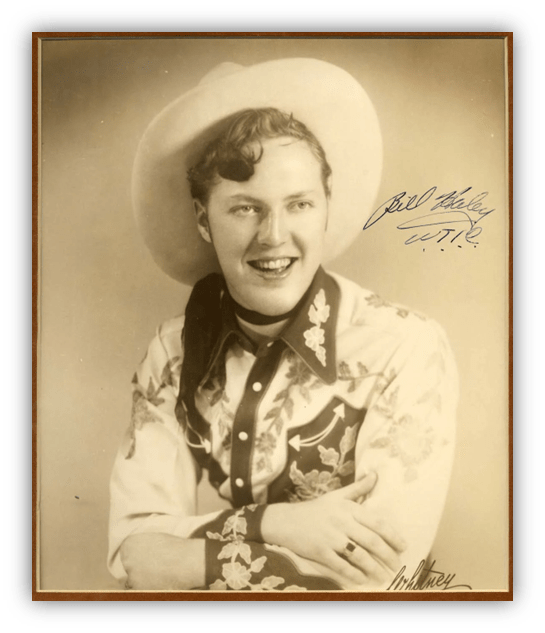"Black and white portrait of a smiling young man in a cowboy hat and embroidered shirt, signed by Bill Haley."