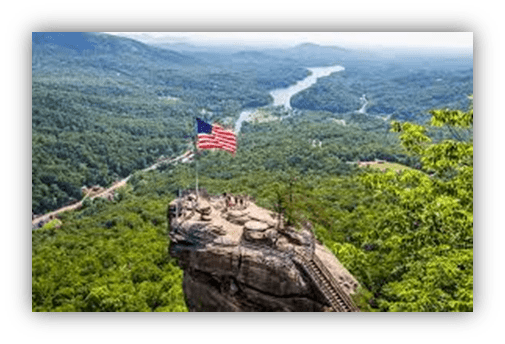 "Scenic view from a rock outcrop with an American flag overlooking a lush valley and river."