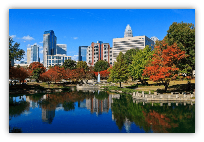 "Charlotte skyline reflecting in a serene park pond with autumn foliage."