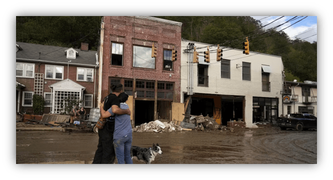 "Couple embracing in front of damaged buildings after flooding, with a dog nearby."