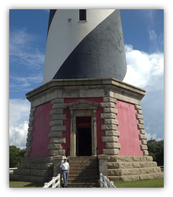 "Colorful lighthouse with a visitor at the entrance against a blue sky."