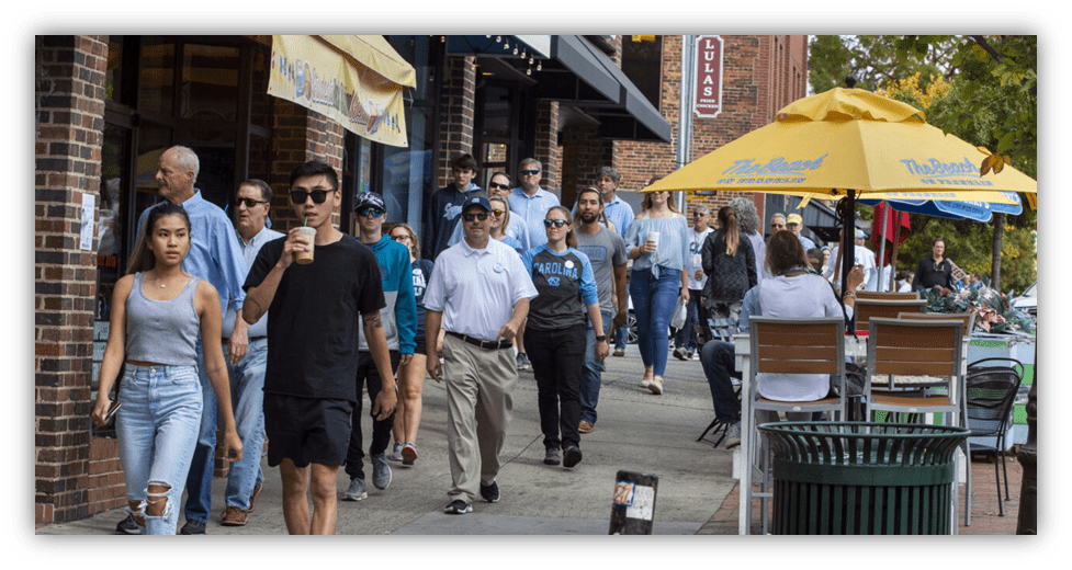 Crowd walking on a busy street with shops and outdoor seating.