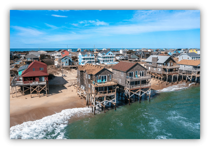 "Colorful beach houses on stilts along the shore, with waves lapping at the sandy beach."