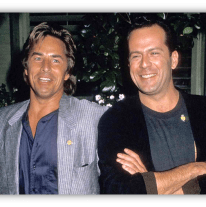 "Two smiling men in stylish outfits posing together outdoors."