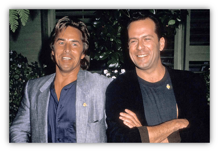 "Two smiling men in stylish outfits posing together outdoors."
