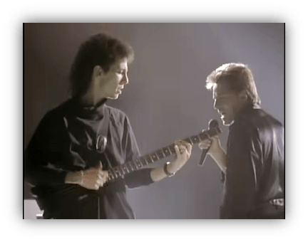 "Two musicians performing on stage, one playing guitar and the other singing into a microphone."